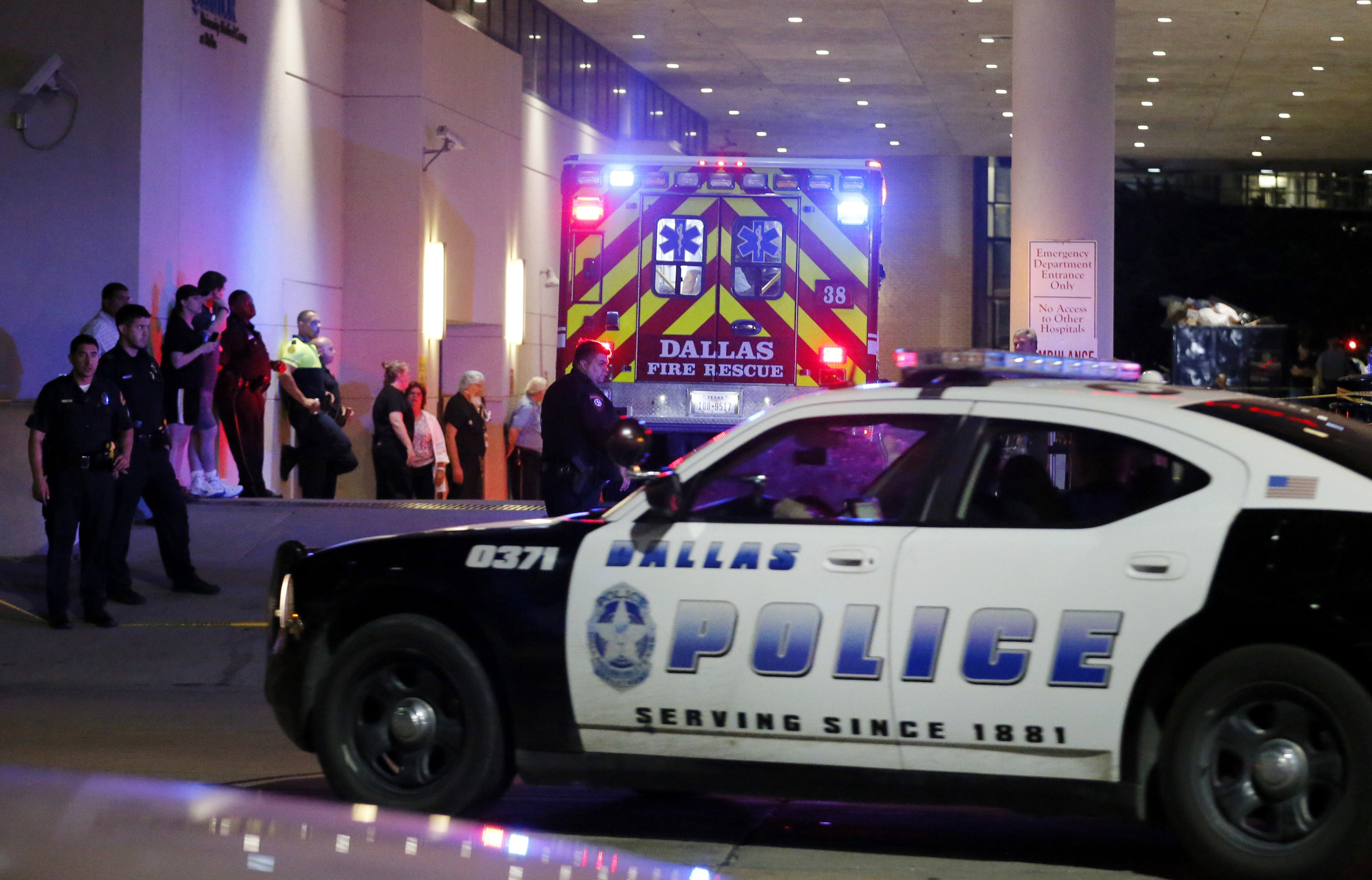 A Dallas police vehicle follows behind an ambulance carrying a patient to the emergency department at Baylor University Medical Center, as police and others stand near the emergency entrance early Friday, July 8, 2016, in Dallas. At least two snipers opened fire on police officers in Dallas on Thursday night during protests over two recent fatal police shootings of black men, police said. (AP Photo/Tony Gutierrez)